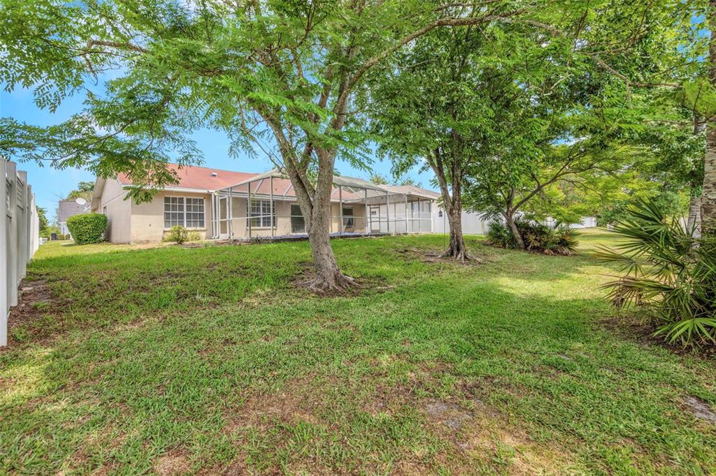 A backyard view of a single-story house with a screened-in patio and large trees — 7919 STARFIRE WAY, NEW PORT RICHEY, FL