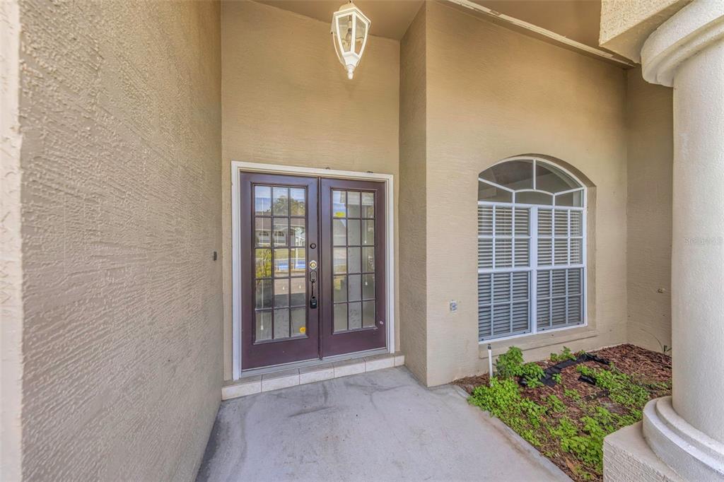 A covered entryway features double glass-paneled doors, a light fixture, and an arched window — 7919 STARFIRE WAY, NEW PORT RICHEY, FL