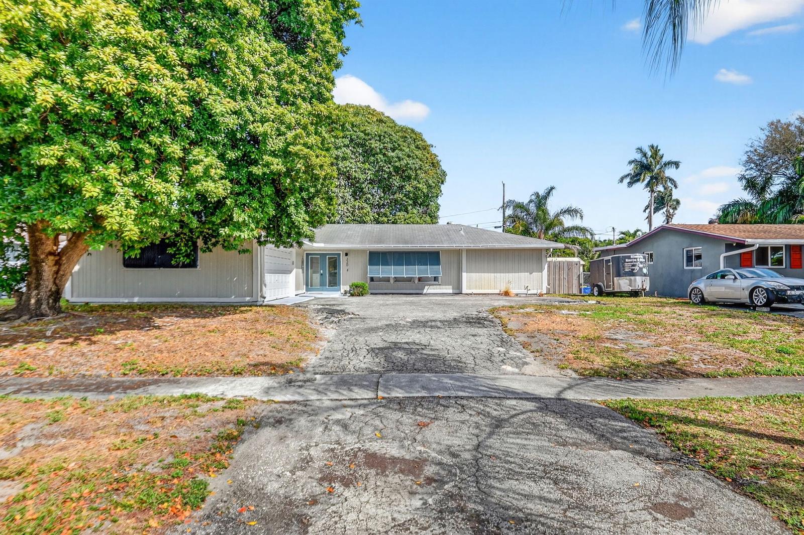 A single-story house with a large tree, a cracked driveway, and a silver car parked — 320 Riverdale Road, Palm Springs FL 33461, PALM SPRINGS, FL