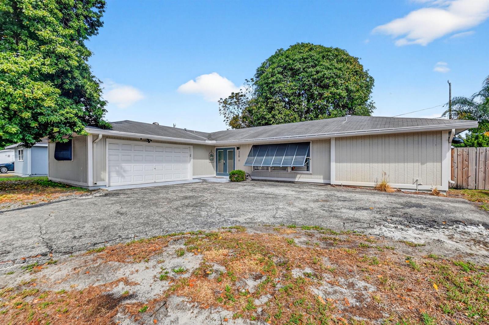 A single-story house with a beige exterior, a two-car garage, and a large asphalt driveway — 320 Riverdale Road, Palm Springs FL 33461, PALM SPRINGS, FL