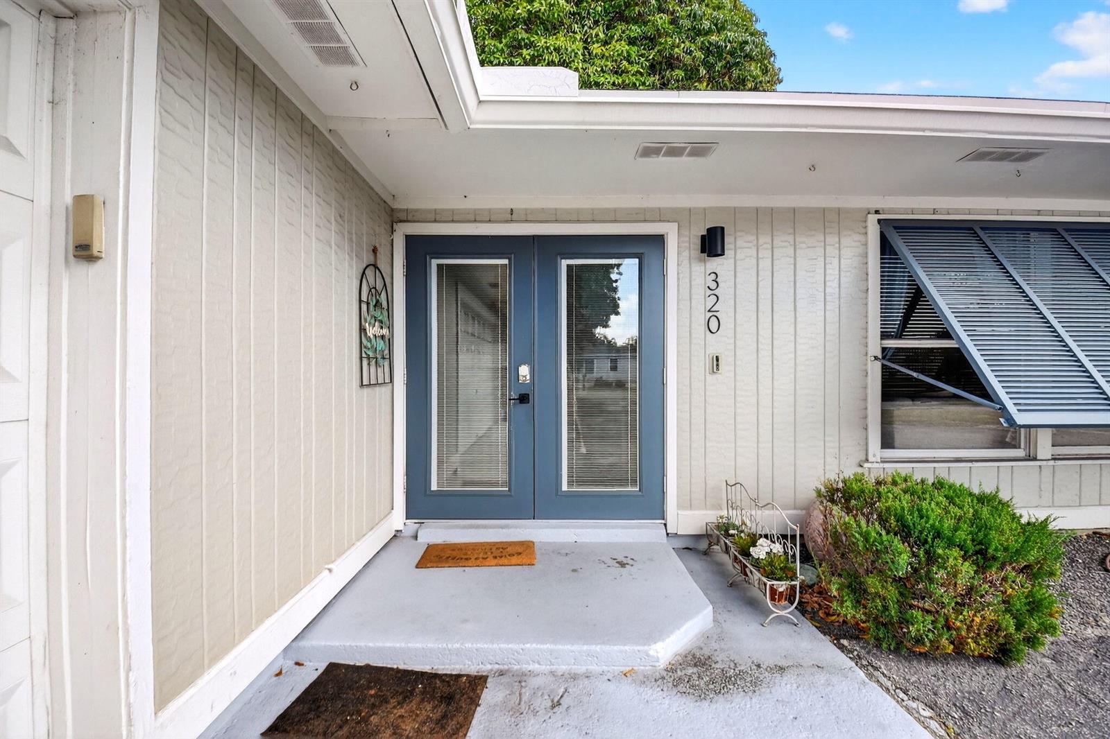The exterior of a house features a blue double door entrance with vertical siding — 320 Riverdale Road, Palm Springs FL 33461, PALM SPRINGS, FL