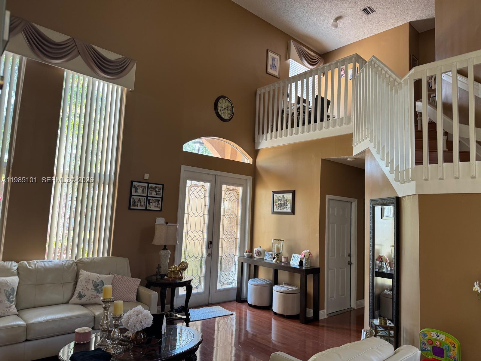A living room features high ceilings, a staircase with a white railing, and hardwood floors — 1661 SE 17th St, Homestead FL 33035, HOMESTEAD, FL