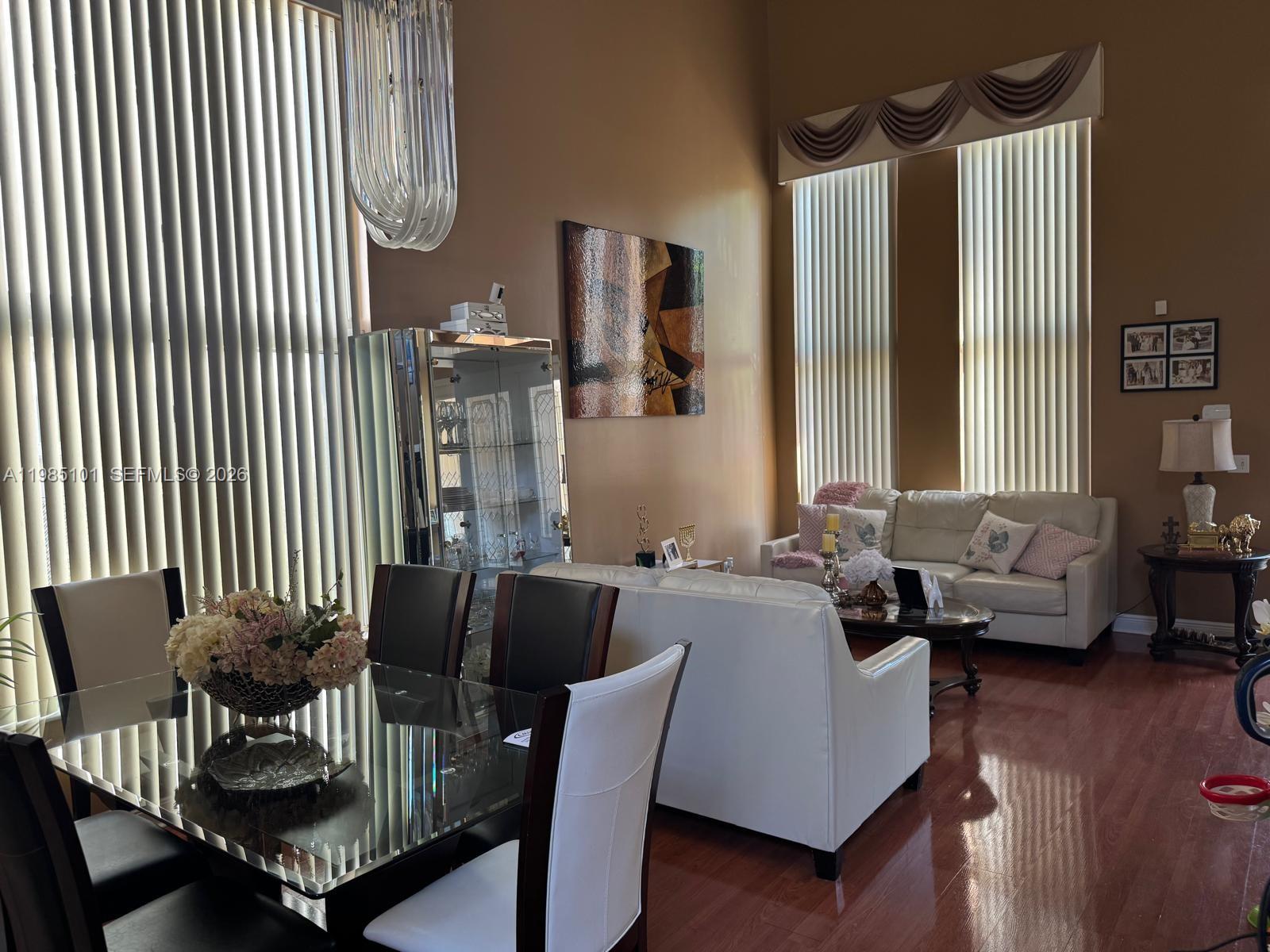 A dining area with a glass table sits in front of a living room with white sofas — 1661 SE 17th St, Homestead FL 33035, HOMESTEAD, FL