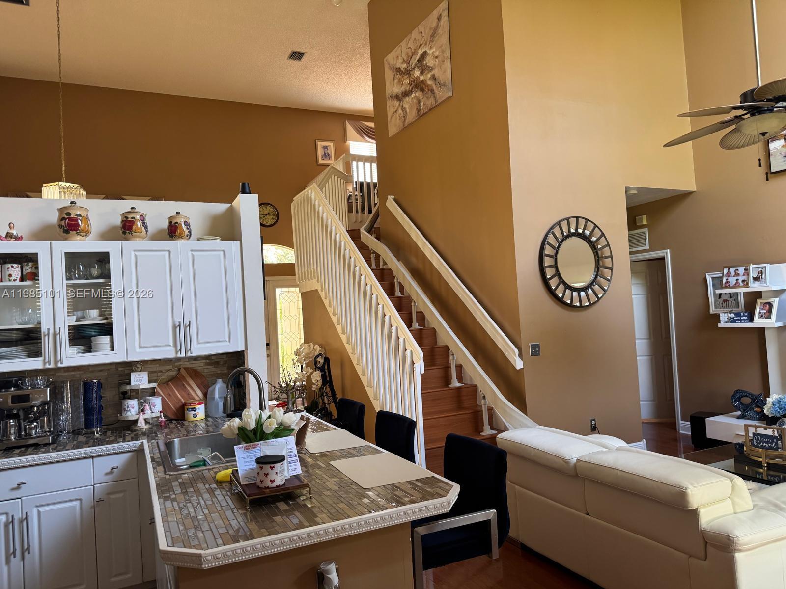 A kitchen with a tiled island and white cabinets overlooks a living area with stairs — 1661 SE 17th St, Homestead FL 33035, HOMESTEAD, FL