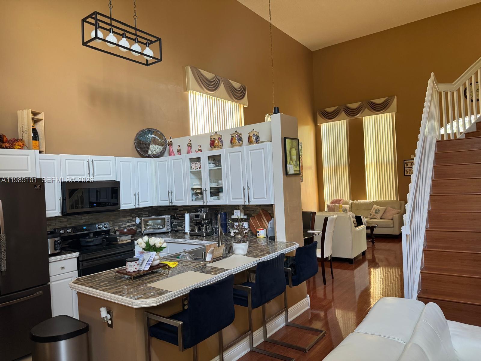 A kitchen with white cabinets and a breakfast bar overlooks a living area with stairs — 1661 SE 17th St, Homestead FL 33035, HOMESTEAD, FL