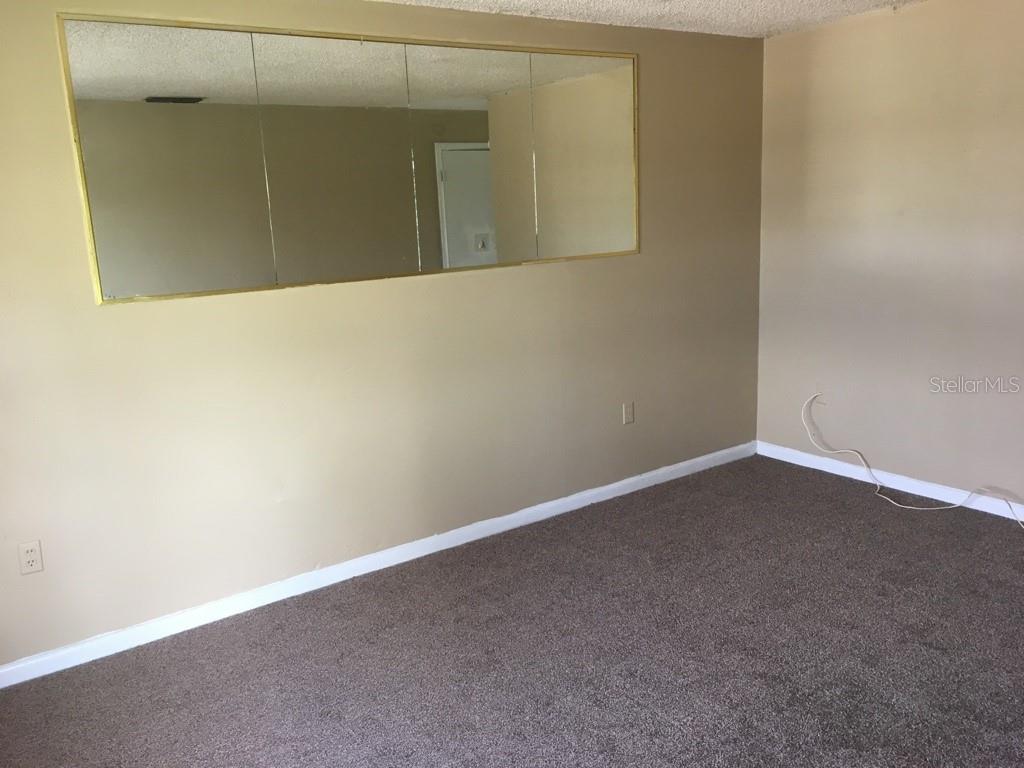 An empty room with brown carpet, beige walls, and a large wall-mounted mirror — 1305-1307 FAIRWAY DRIVE, LAKELAND, FL