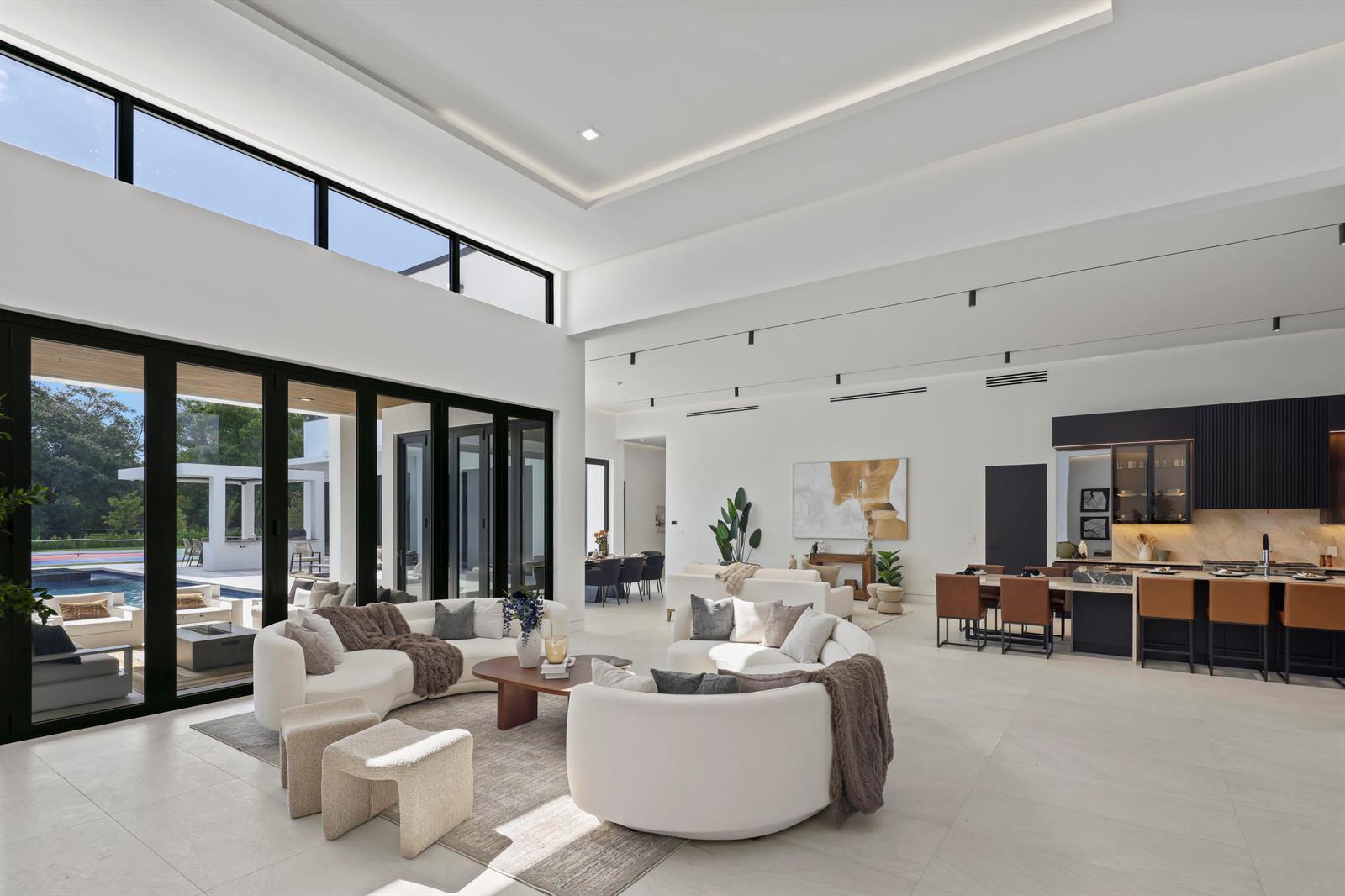 A spacious open-concept living area features white curved sofas, a modern kitchen, and floor-to-ceiling windows — 6676 NW 66th Way, Parkland FL 33067, PARKLAND, FL