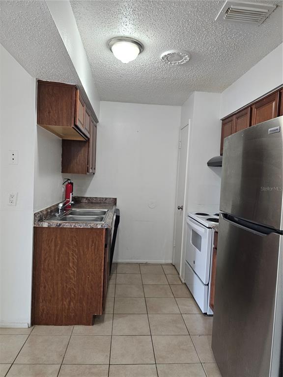 A kitchen features wood cabinets, a stainless steel refrigerator, a white stove, and tile flooring — 247 THORN TREE PLACE UNIT 247, BRANDON, FL