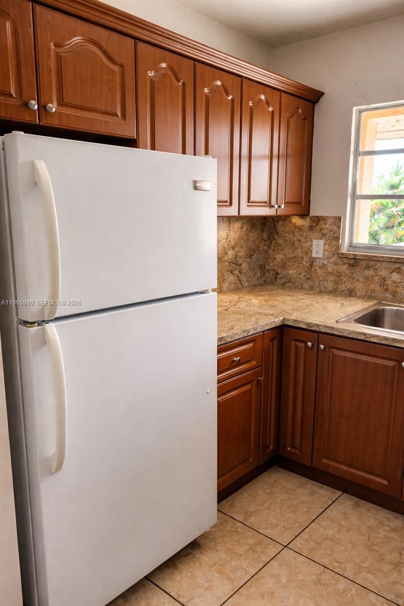 A kitchen features wood cabinets, a white refrigerator, and tan stone-look countertops and flooring — 6850 W 14th Ct # A15, Hialeah FL 33014, HIALEAH, FL