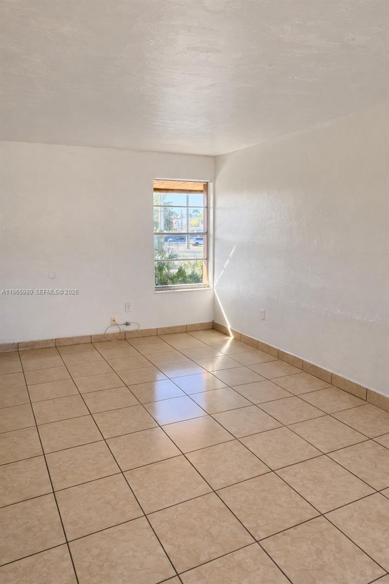 An empty room features white walls, tan tiled flooring, and a single window — 6850 W 14th Ct # A15, Hialeah FL 33014, HIALEAH, FL