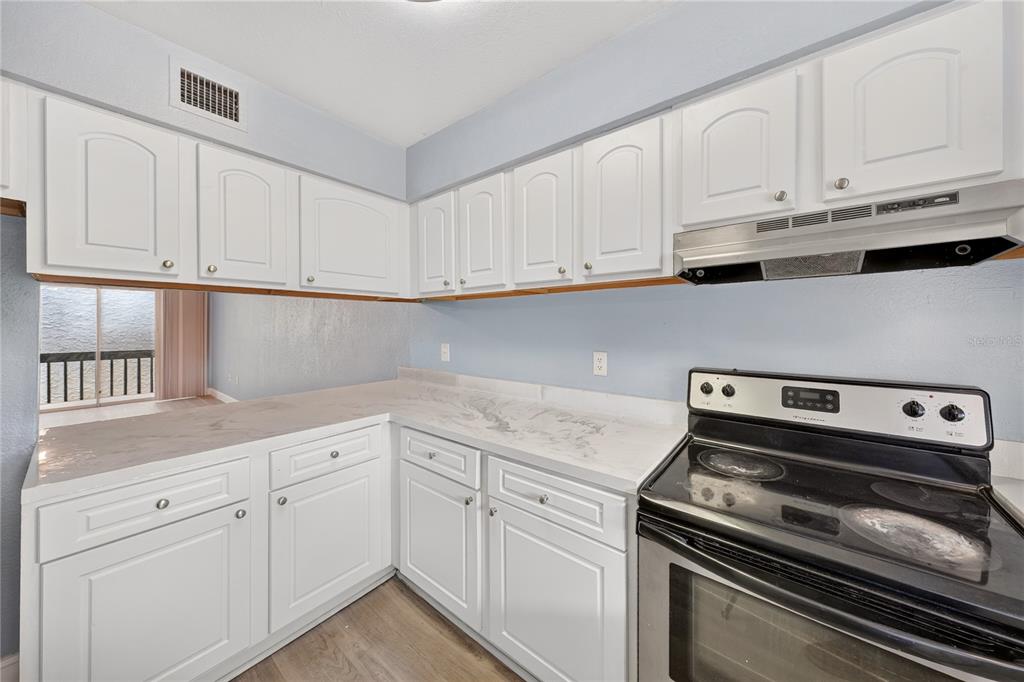A kitchen features white cabinets, light-colored countertops, a black electric range, and light blue walls — 4223 S. SEMORAN BLVD UNIT 6, ORLANDO, FL