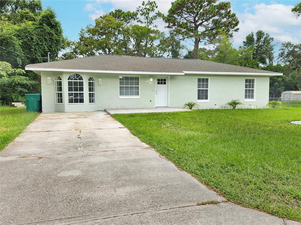 A single-story house with light green stucco siding, a concrete driveway, and a shingled roof — 1001 JONES AVENUE, INVERNESS, FL