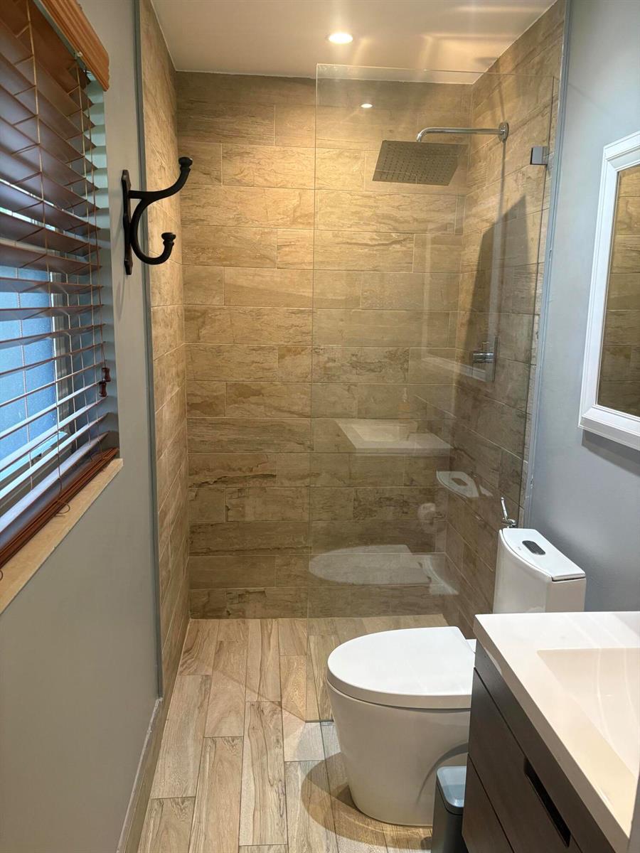 A bathroom features a walk-in shower with wood-look tile, a glass panel, and a toilet — 2565 Meadow Road, West Palm Beach FL 33406, WEST PALM BEACH, FL