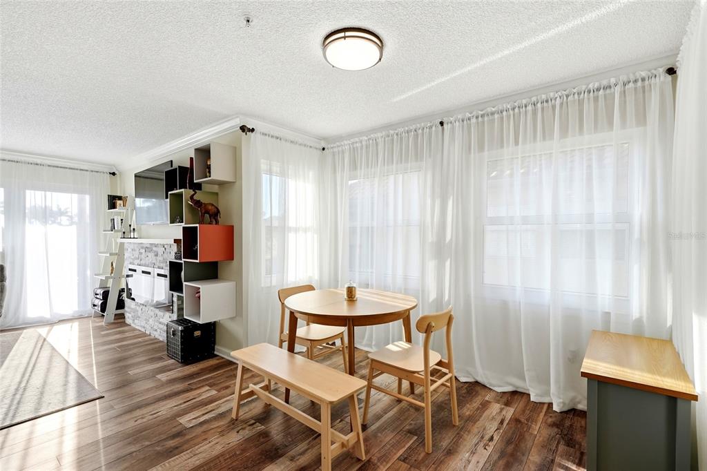 A dining area with a round table, wooden chairs, a bench, and sheer white curtains — 2400 FEATHER SOUND DRIVE UNIT 1428, CLEARWATER, FL