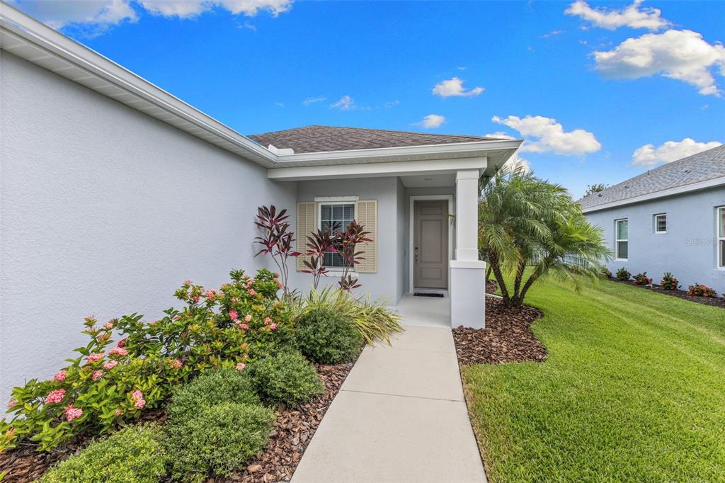 A concrete walkway leads to the front entrance of a light-colored house with landscaping — 13840 OLD CREEK COURT, PARRISH, FL
