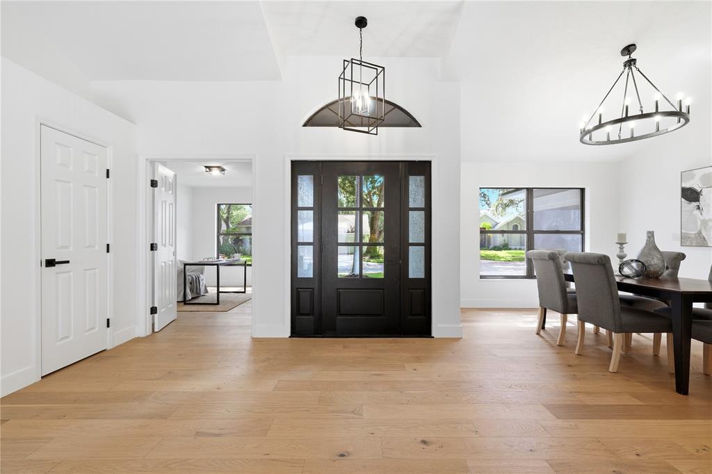 A bright entryway with light wood floors, a dark front door, and two hanging light fixtures — 3040 WINDRIDGE OAKS DRIVE, PALM HARBOR, FL