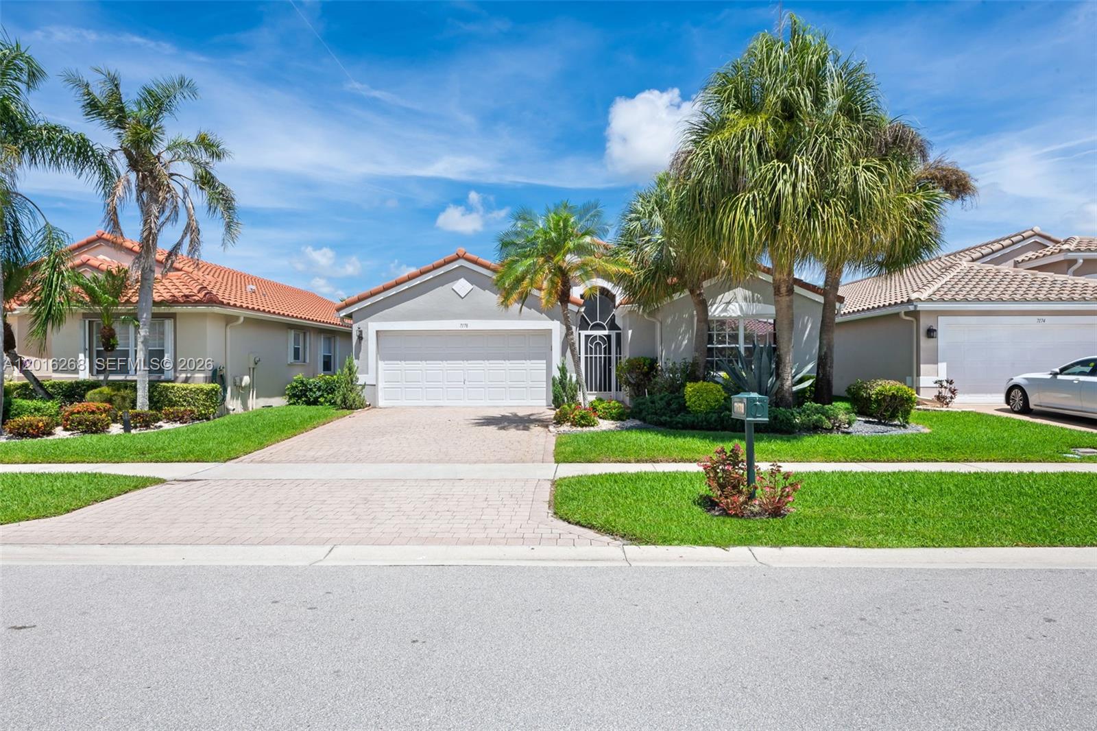 A single-story suburban house features a paved driveway, a two-car garage, and several palm trees — 7178 Haviland Circle, Boynton Beach FL 33437, BOYNTON BEACH, FL