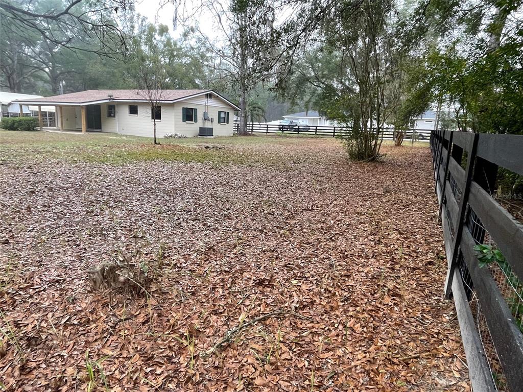A beige house with a covered patio sits on a large lot with leaf-covered ground — 4486 SW 159TH COURT, OCALA, FL