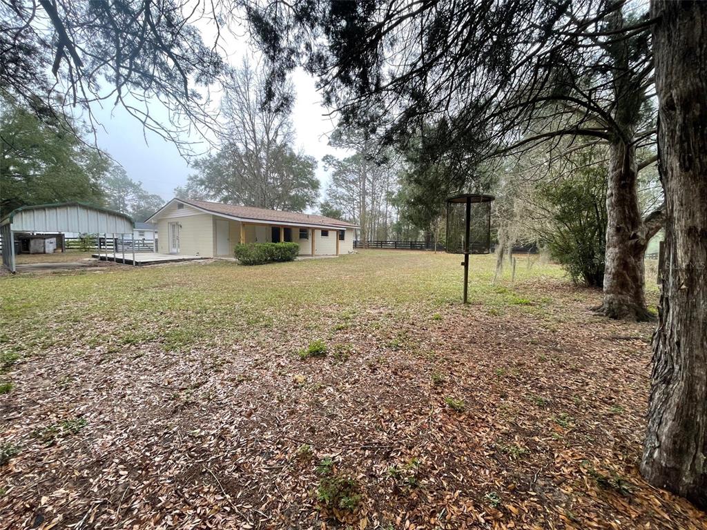A single-story house with a metal carport sits on a large, tree-filled grassy lot — 4486 SW 159TH COURT, OCALA, FL