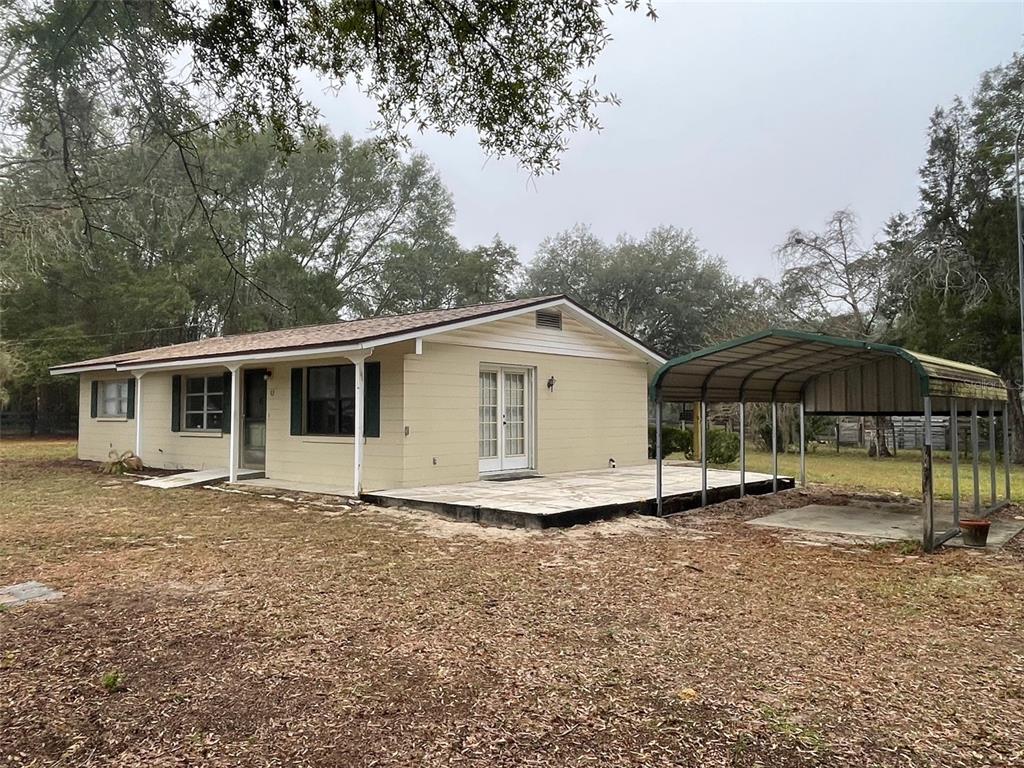 A light-colored, single-story house with a patio and a metal carport in the yard — 4486 SW 159TH COURT, OCALA, FL