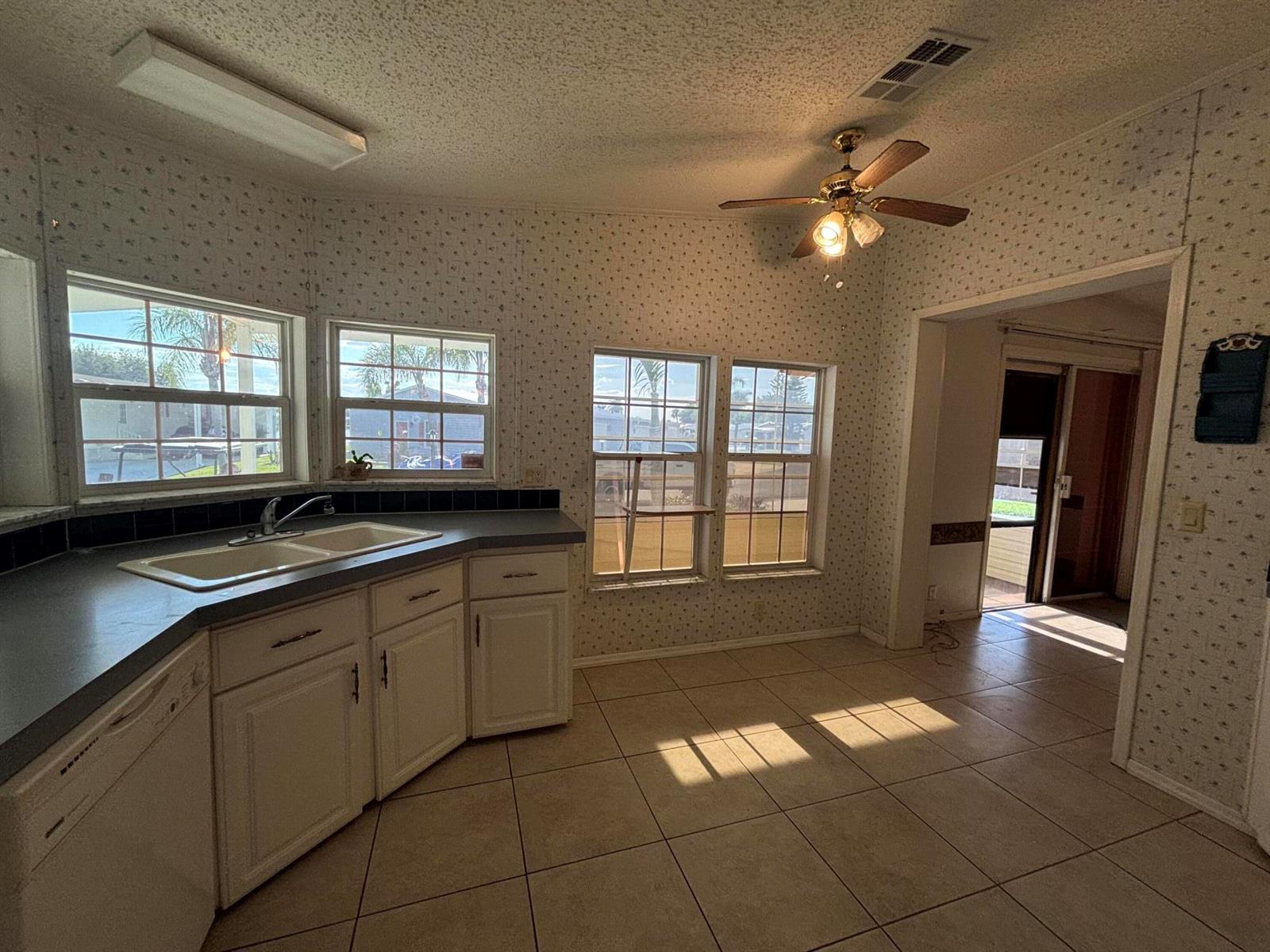 A kitchen with white cabinets, tile flooring, wallpaper, and multiple windows overlooking an outdoor area — 1621 SW 35th Circle, Okeechobee FL 34974, OKEECHOBEE, FL