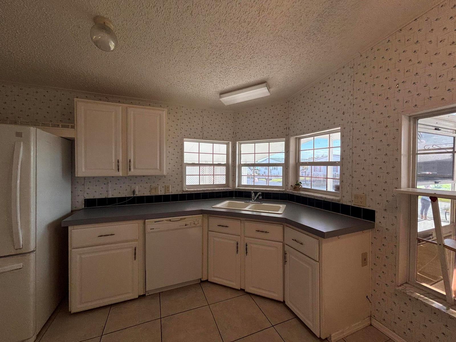 A kitchen features white cabinets, gray countertops, tiled floors, and wallpapered walls with corner windows — 1621 SW 35th Circle, Okeechobee FL 34974, OKEECHOBEE, FL