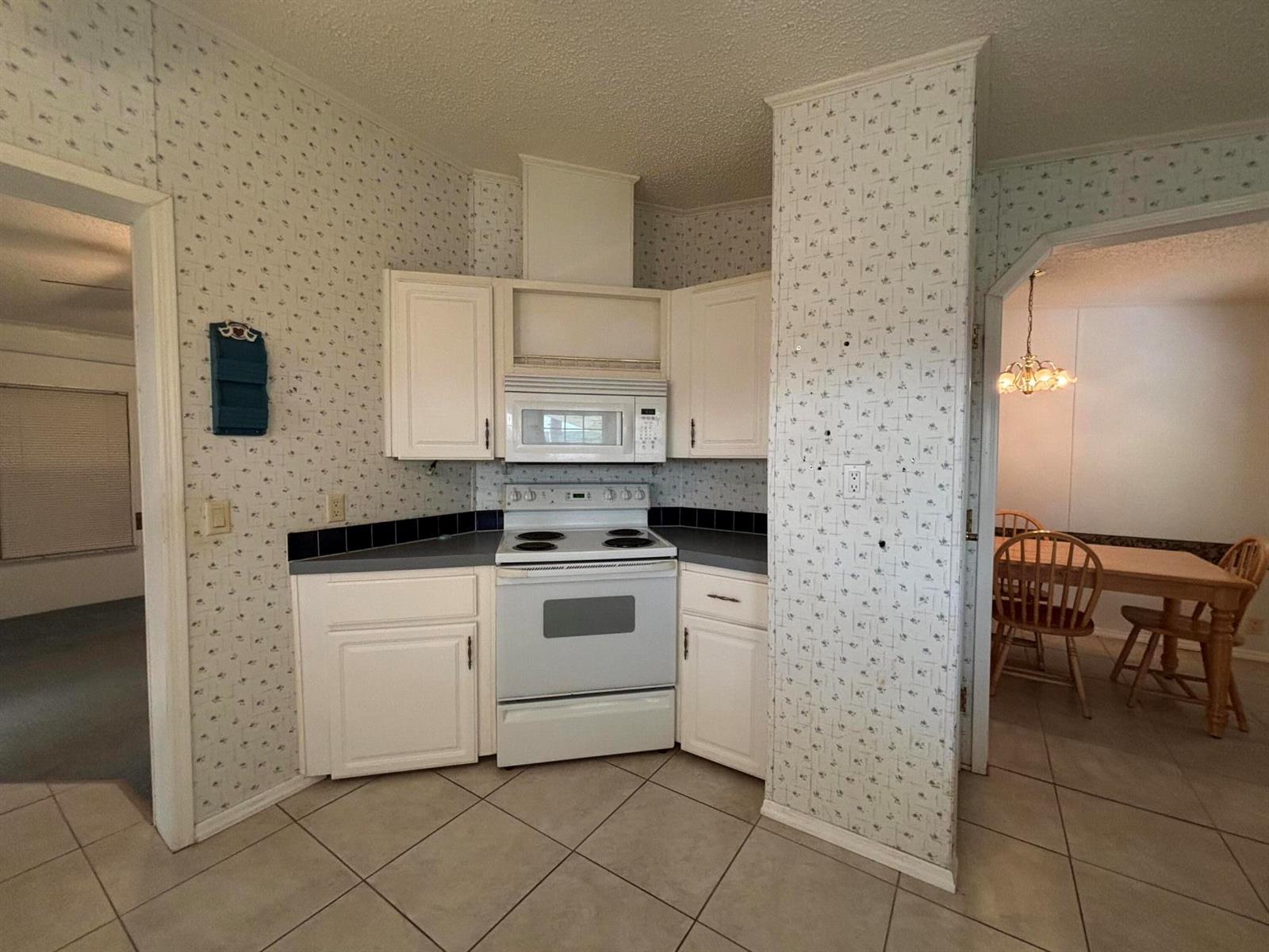 A kitchen features white cabinets, a white stove, a microwave, and patterned wallpaper — 1621 SW 35th Circle, Okeechobee FL 34974, OKEECHOBEE, FL