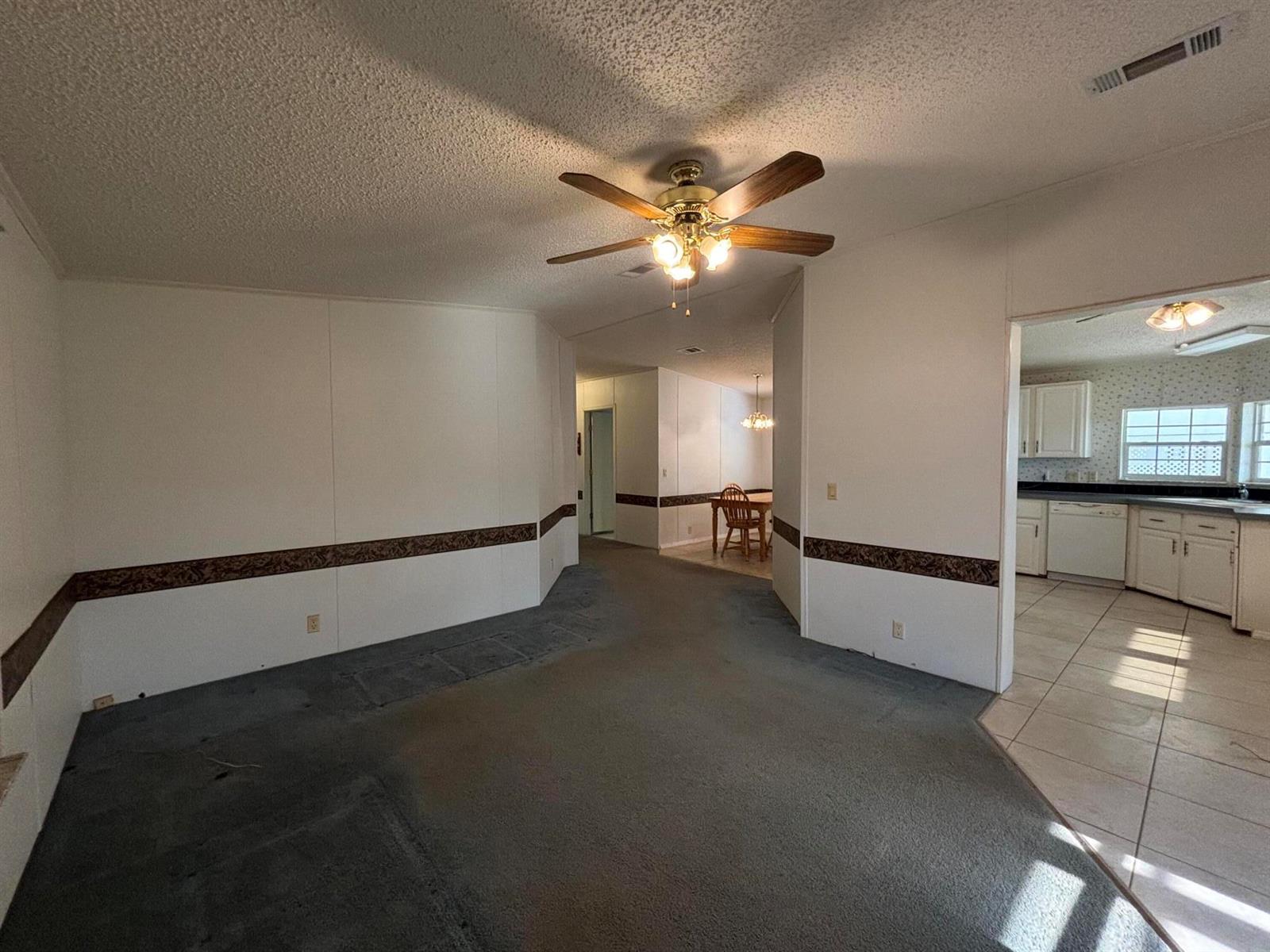 A living room with gray carpet, a ceiling fan, and a view into the kitchen — 1621 SW 35th Circle, Okeechobee FL 34974, OKEECHOBEE, FL
