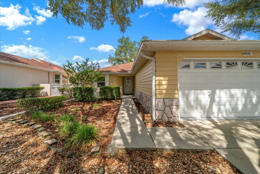 A single-story house with yellow siding, a stone base, and a concrete walkway to the entrance — 9040 SW 91ST TERRACE, OCALA, FL