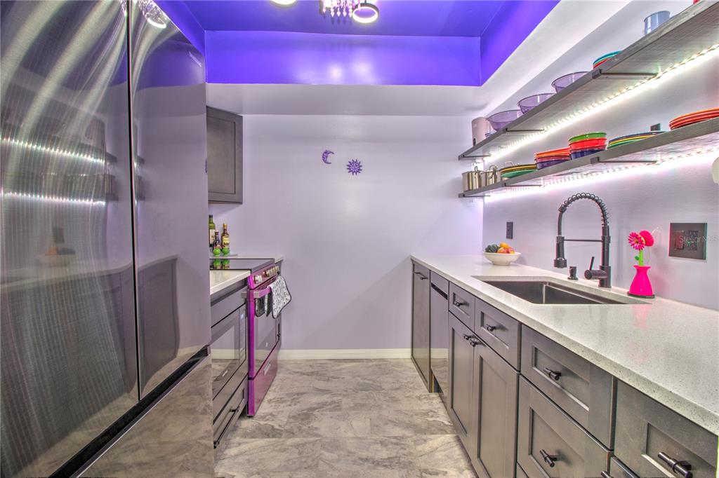 A galley kitchen features dark gray cabinets, purple accents, open shelving, and stainless steel appliances — 1640 NE 40TH AVENUE UNIT 204, OCALA, FL
