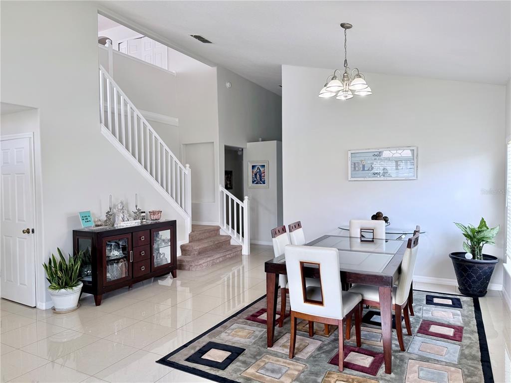 A dining room with a glass-topped table, white chairs, tile floors, and a staircase — 142 BRIGHTVIEW DRIVE, LAKE MARY, FL