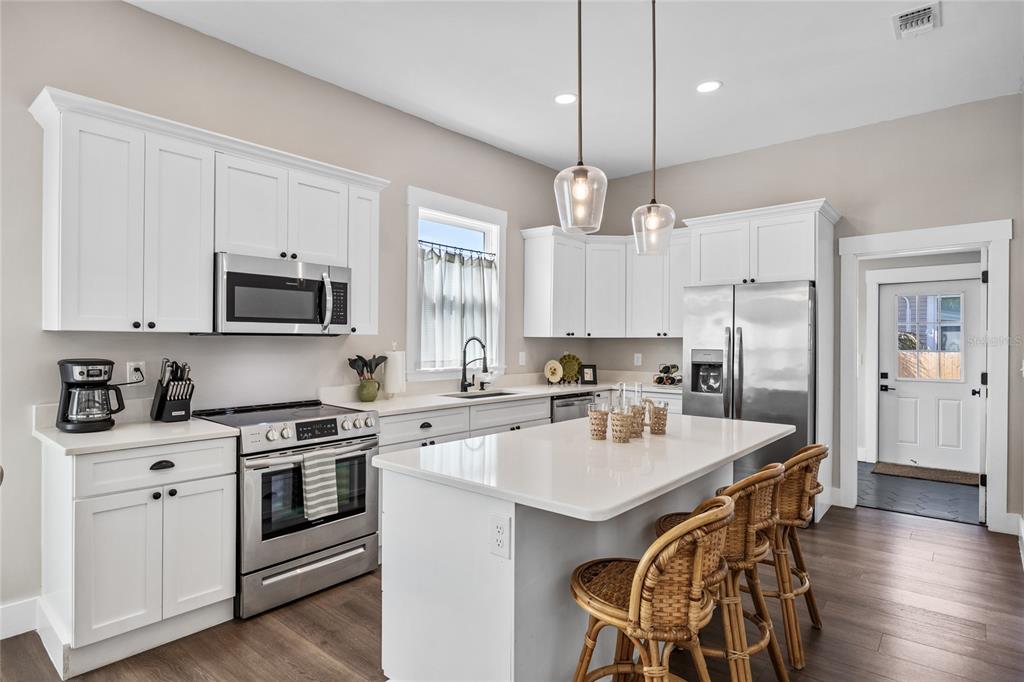 A kitchen features white cabinets, stainless steel appliances, a quartz island, and rattan bar stools — 3002 N 16TH STREET, TAMPA, FL