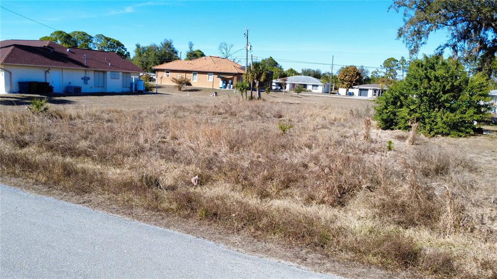 A vacant, grassy residential lot sits next to existing houses under a clear blue sky — LORANZA AVENUE, NORTH PORT, FL