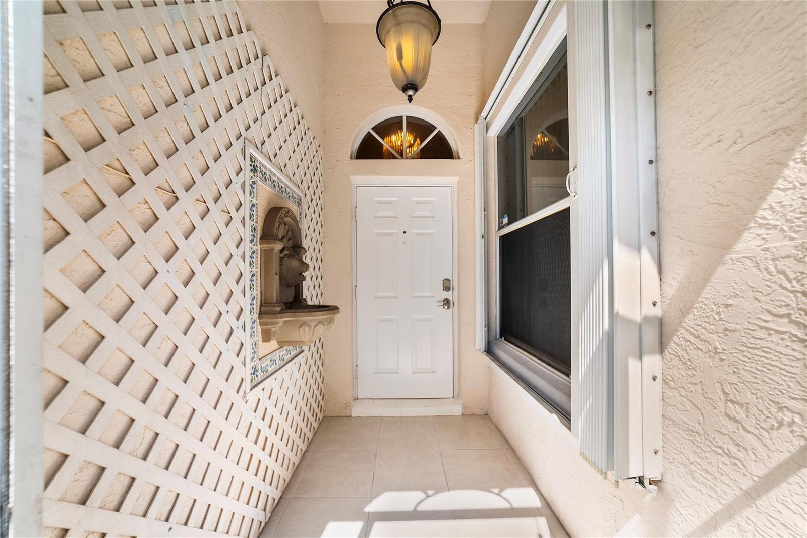 A white front door sits in a tiled entryway with a wall fountain and lattice — 5021 S La Sedona Circle, Delray Beach FL 33484, DELRAY BEACH, FL