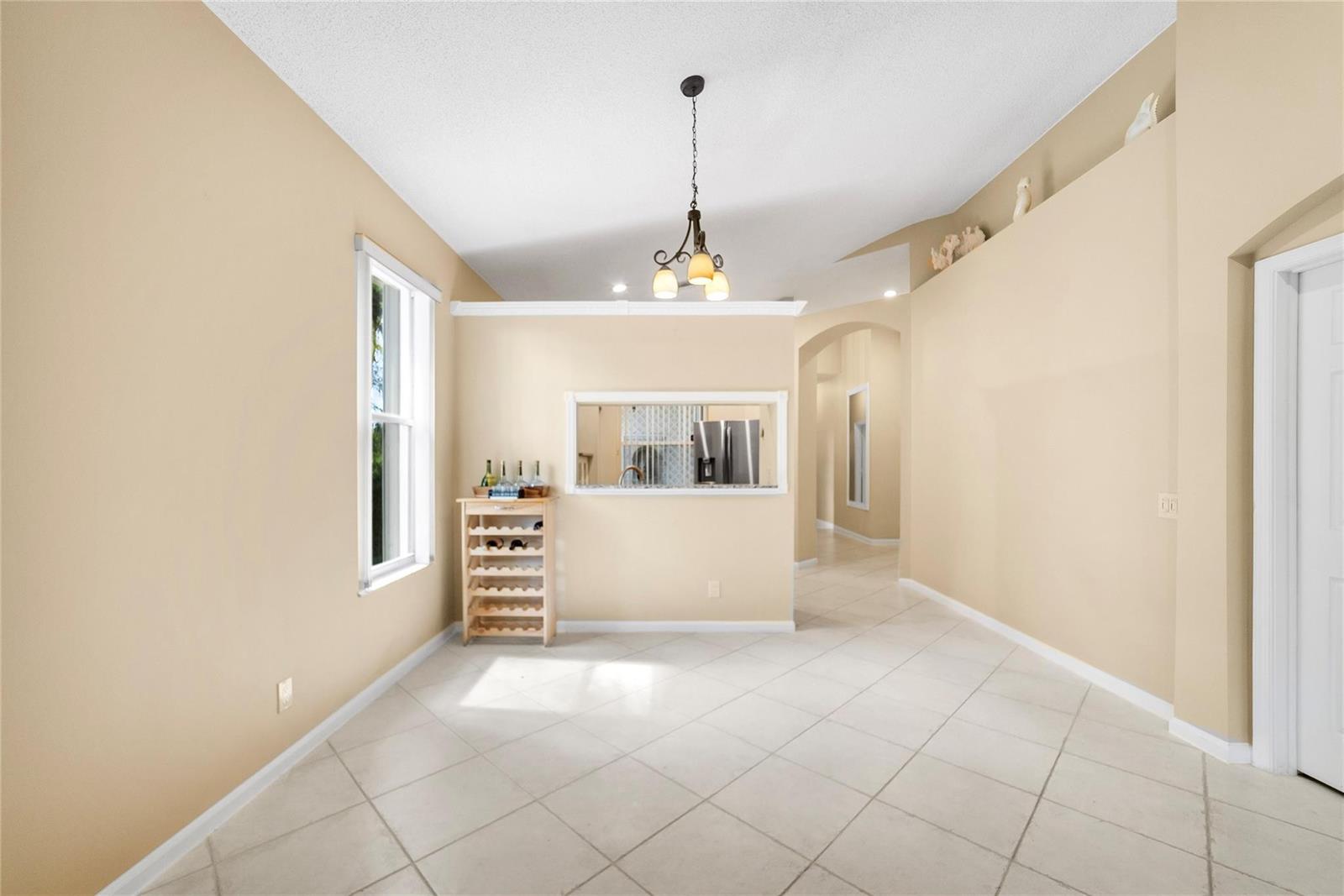 A dining area features beige walls, tile flooring, a chandelier, and a kitchen pass-through window — 5021 S La Sedona Circle, Delray Beach FL 33484, DELRAY BEACH, FL