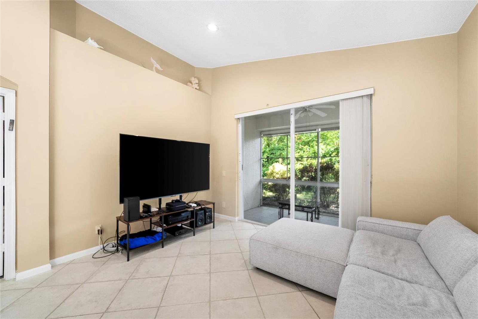 A living room features a large television on a stand, light tile floors, and sliding doors — 5021 S La Sedona Circle, Delray Beach FL 33484, DELRAY BEACH, FL