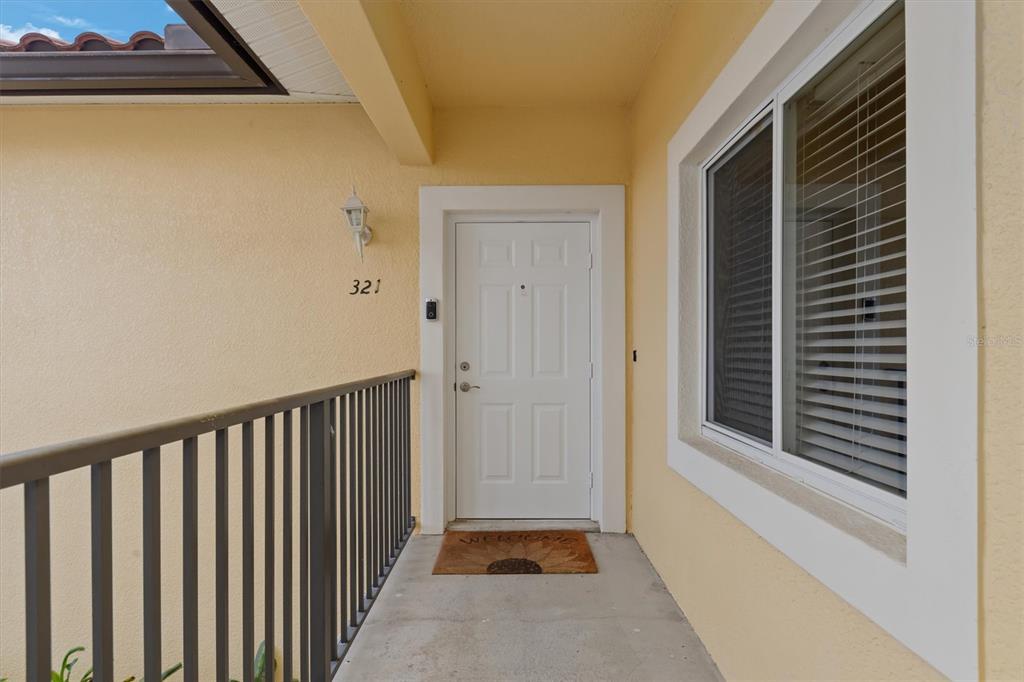 A white front door with a welcome mat sits on a covered outdoor walkway — 7196 N PLUM TREE UNIT 321, PUNTA GORDA, FL