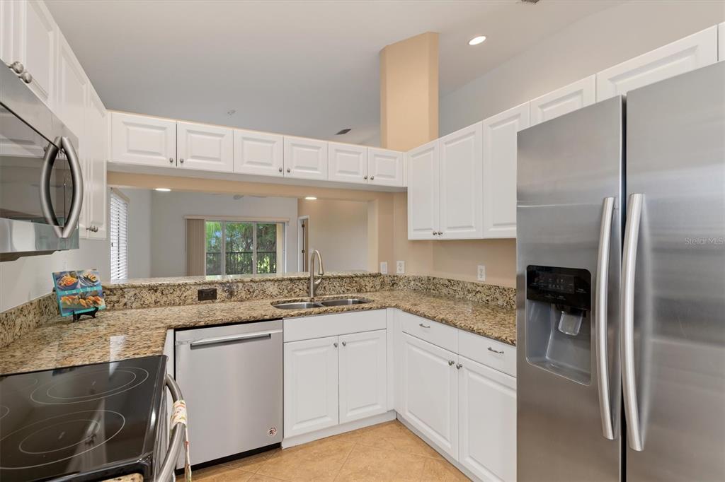 A kitchen features white cabinets, granite countertops, stainless steel appliances, and a pass-through window — 7196 N PLUM TREE UNIT 321, PUNTA GORDA, FL