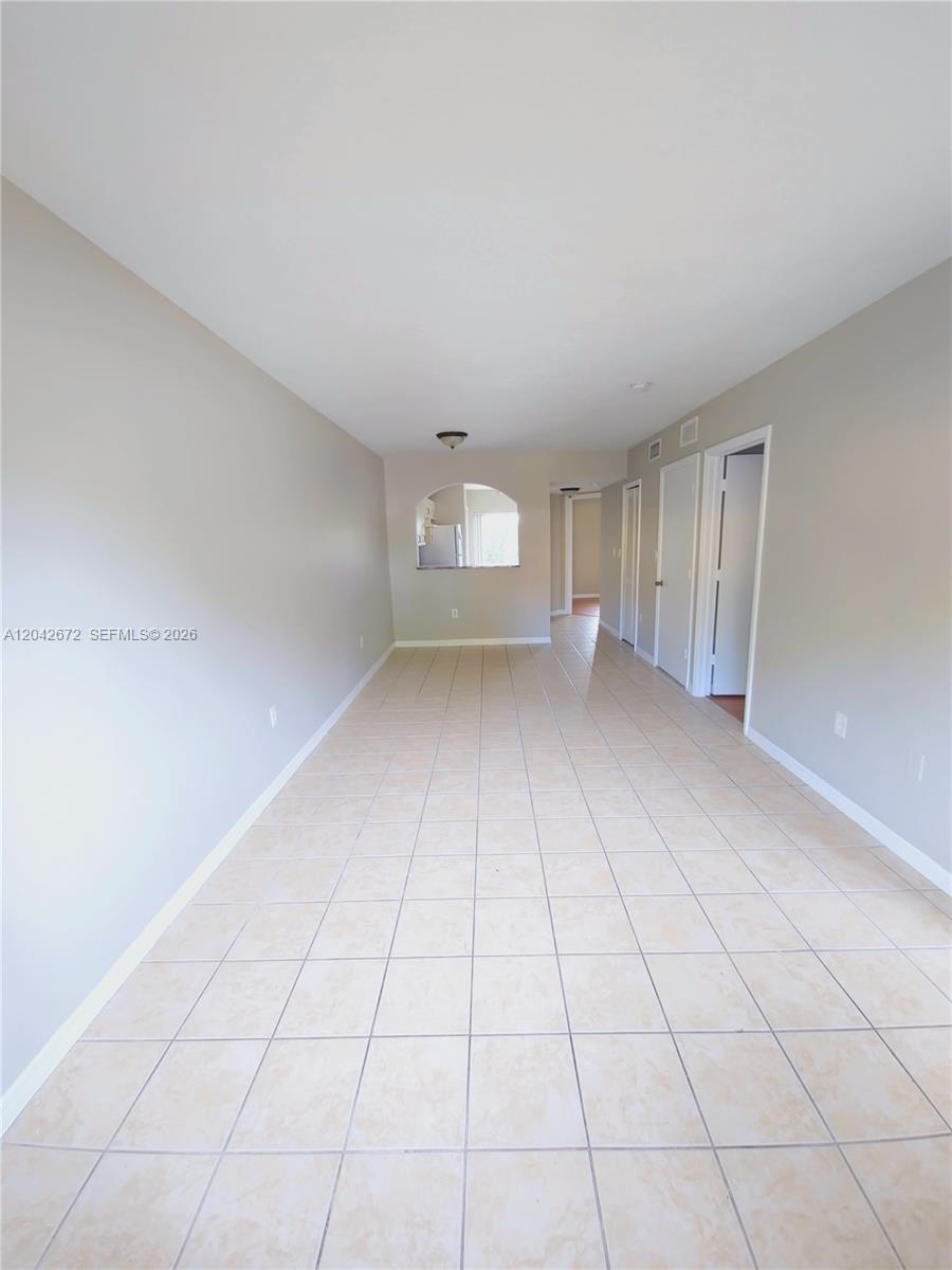 This room features light-colored tile flooring, beige walls, and an arched opening to a kitchen — 990 NE 33rd Ter # 102, Homestead FL 33033, HOMESTEAD, FL