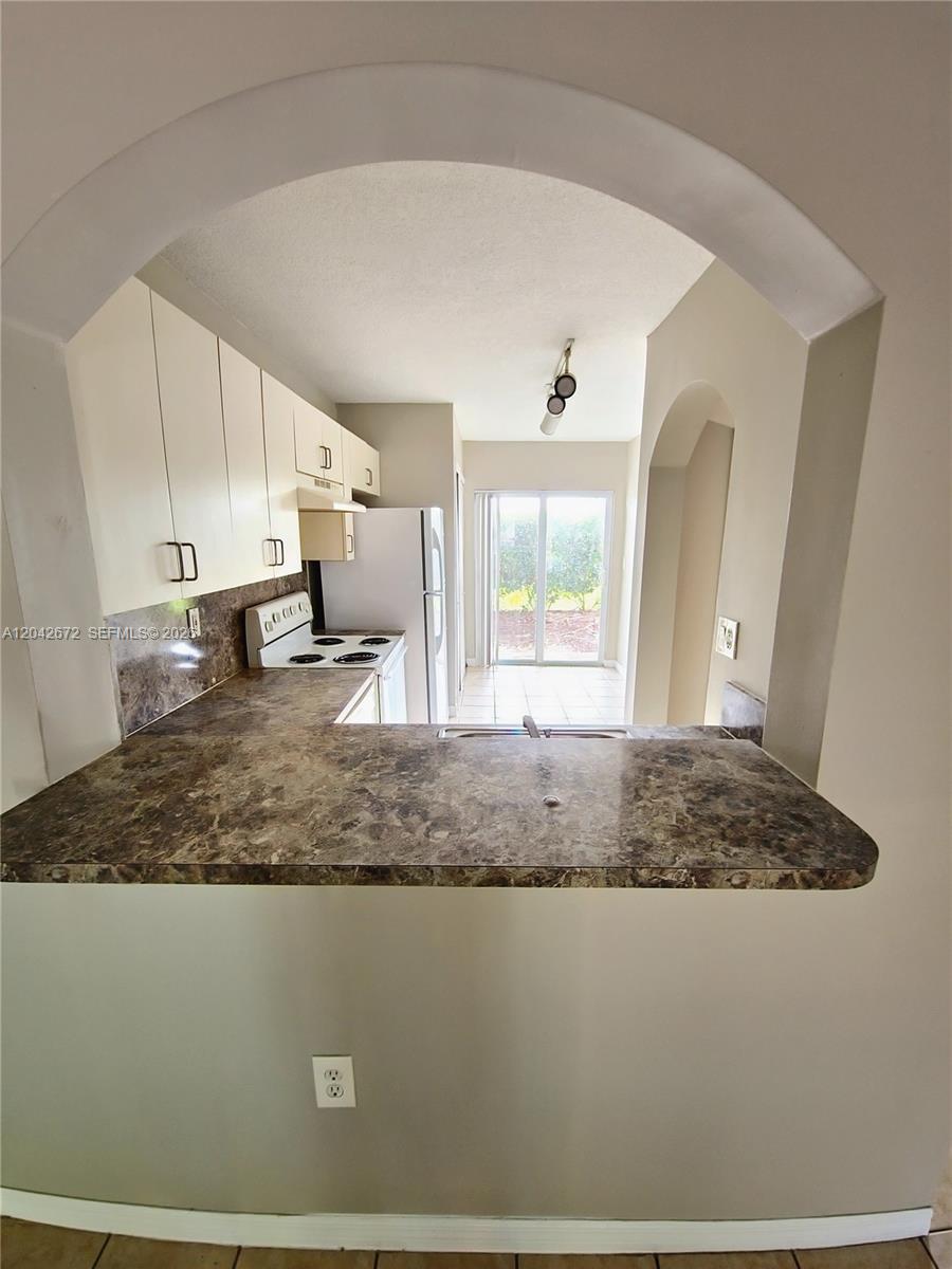 A kitchen with white cabinets, a marble-patterned countertop, and a sliding glass door — 990 NE 33rd Ter # 102, Homestead FL 33033, HOMESTEAD, FL