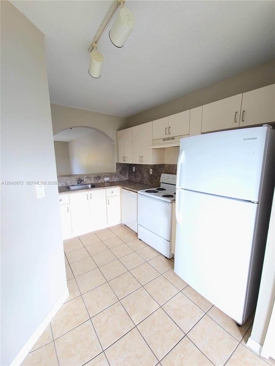 This kitchen features white cabinets, white appliances, tile flooring, and a pass-through window — 990 NE 33rd Ter # 102, Homestead FL 33033, HOMESTEAD, FL