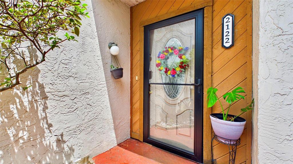 A front entrance features a glass storm door, wood paneling, and potted plants — 2122 TARPON LANDINGS DRIVE, TARPON SPRINGS, FL