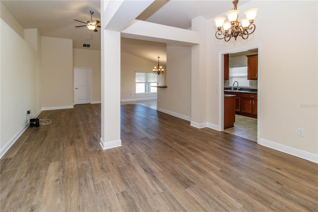 An open-concept living and dining area features wood-look flooring, white walls, and a kitchen doorway — 13541 NITI DRIVE, HUDSON, FL