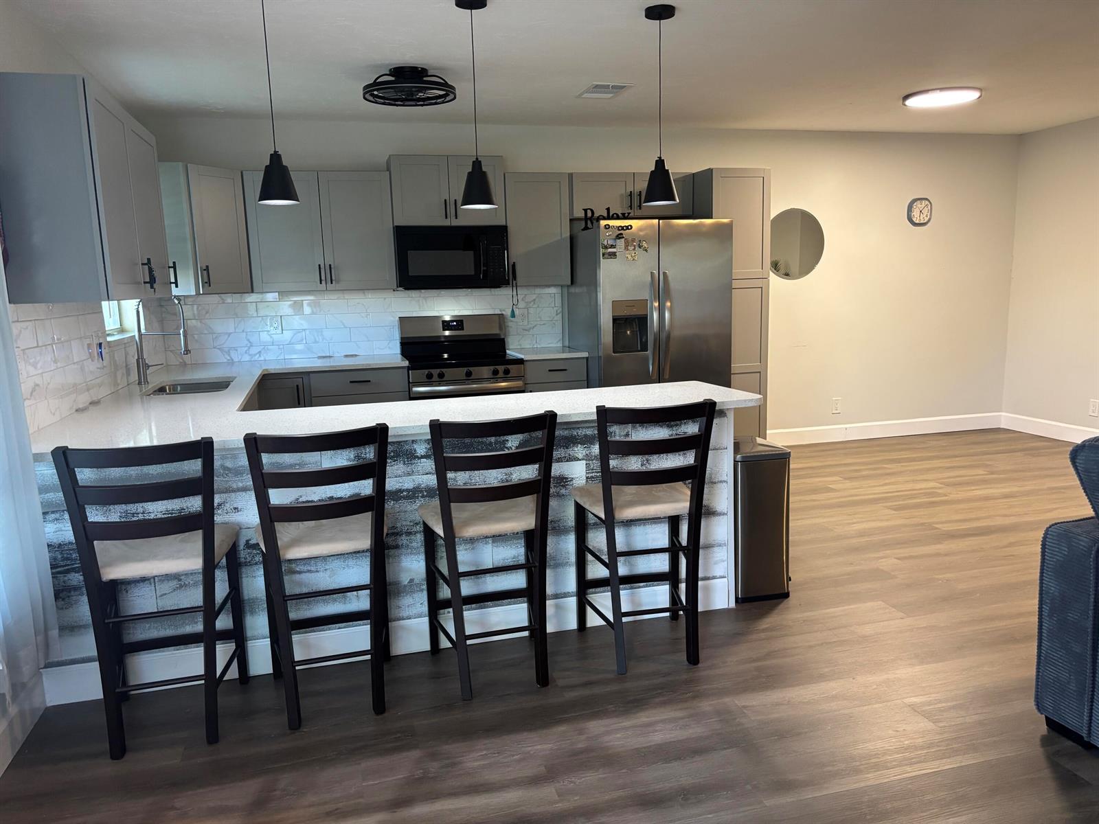 A kitchen features gray cabinets, stainless steel appliances, a white countertop, and four bar stools — 211 Country Lane # C, Boynton Beach FL 33435, BOYNTON BEACH, FL