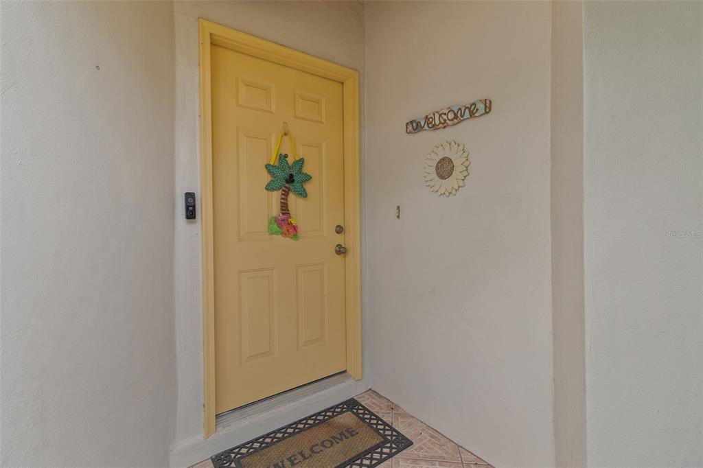 A yellow front door with a palm tree decoration is set in a beige alcove — 235 SOUTHAMPTON LANE UNIT 276, VENICE, FL