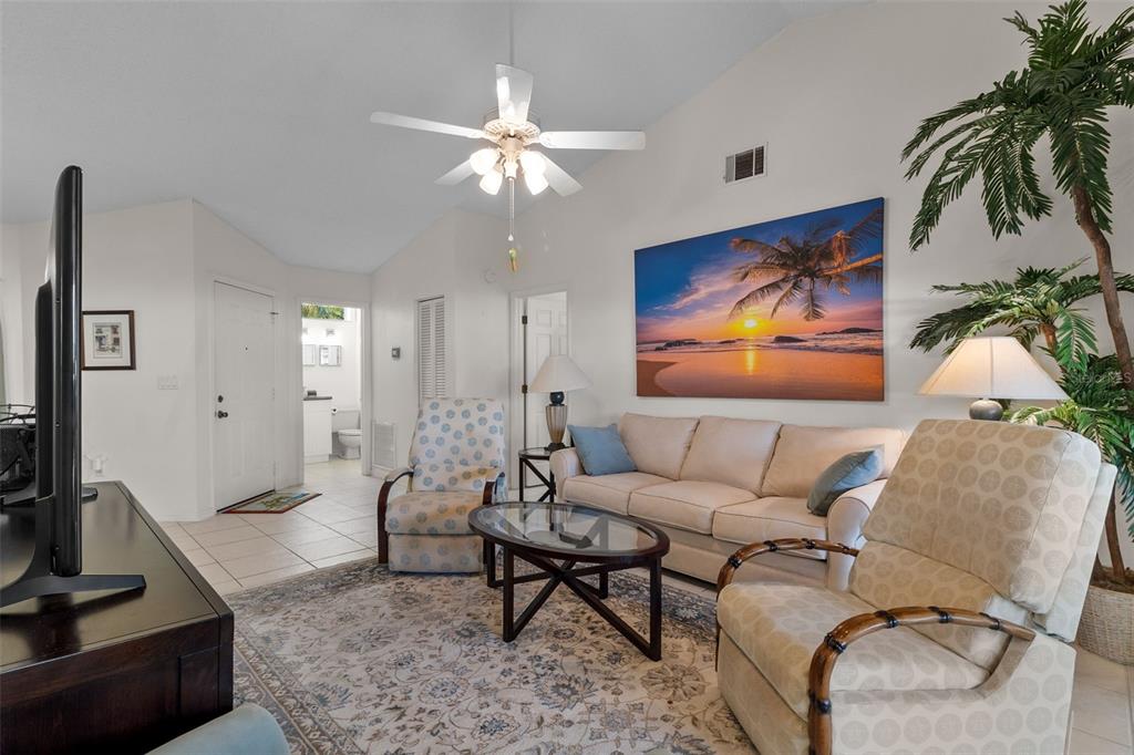 A living room features a beige sofa, two patterned armchairs, a glass coffee table, and artwork — 235 SOUTHAMPTON LANE UNIT 276, VENICE, FL