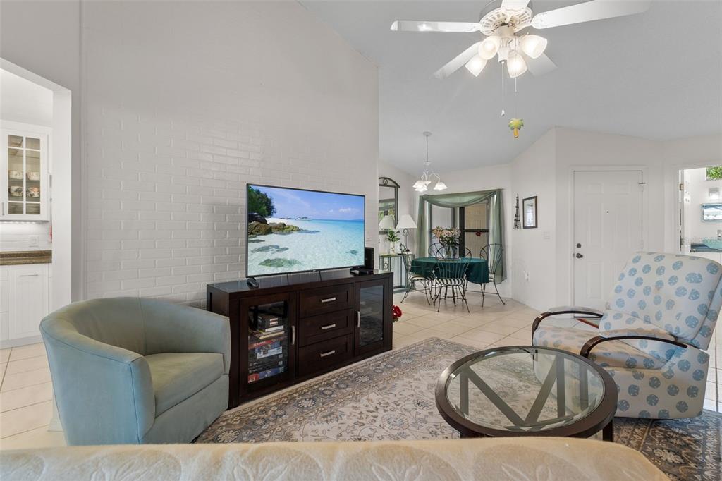 A living room with a white brick wall, television console, and dining area beyond — 235 SOUTHAMPTON LANE UNIT 276, VENICE, FL