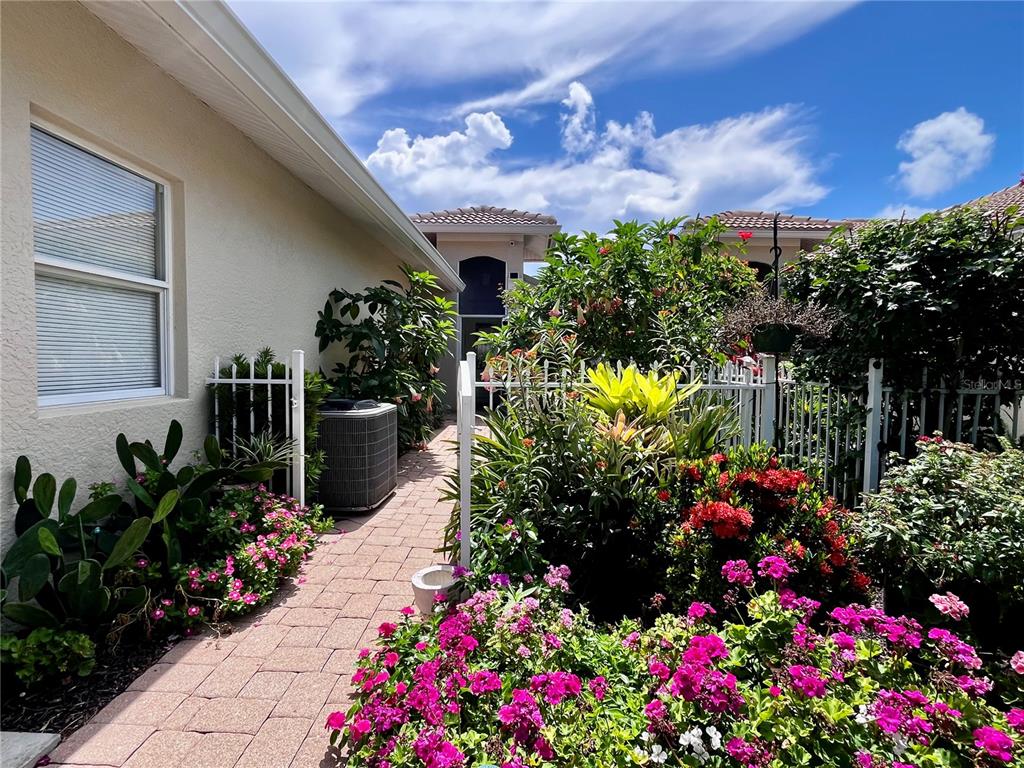 A paved walkway leads past a house exterior and lush garden toward a gated entrance — 1078 TOPELIS DRIVE, ENGLEWOOD, FL