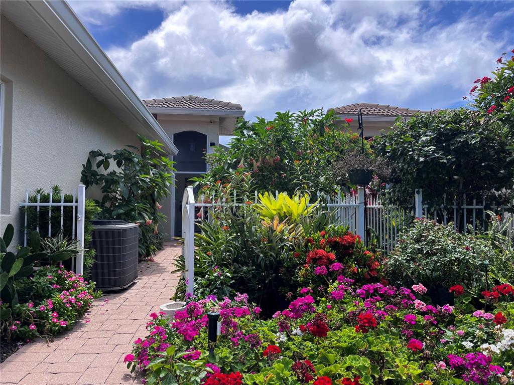 A brick walkway leads to a home entrance surrounded by lush, colorful garden landscaping — 1078 TOPELIS DRIVE, ENGLEWOOD, FL