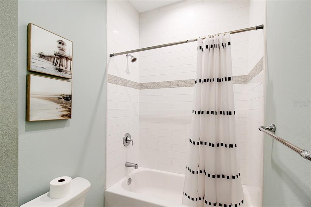 A bathroom features a white tiled shower-tub combination, a toilet, and two framed wall pictures — 14550 SCHOFIELD ROAD UNIT 3, PORT CHARLOTTE, FL